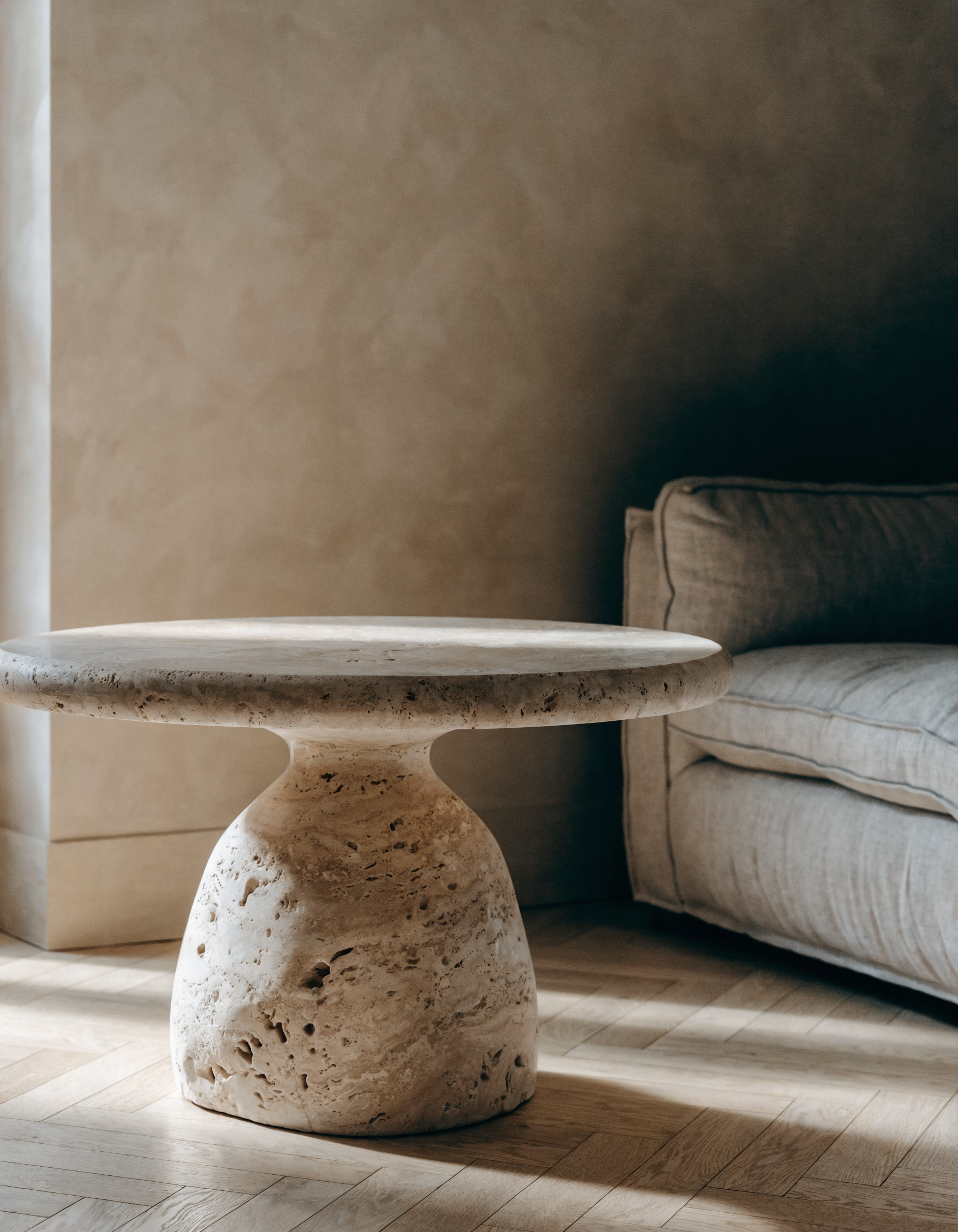 The Travertine Drum Coffee Table in warm living room — herringbone oak floor, polished plaster walls