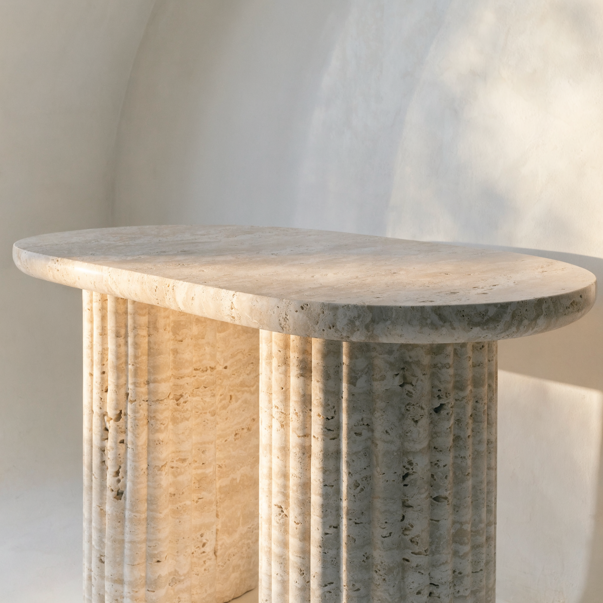 The Fluted Oval Coffee Table in warm ivory travertine — fluted cylindrical column legs, honed finish