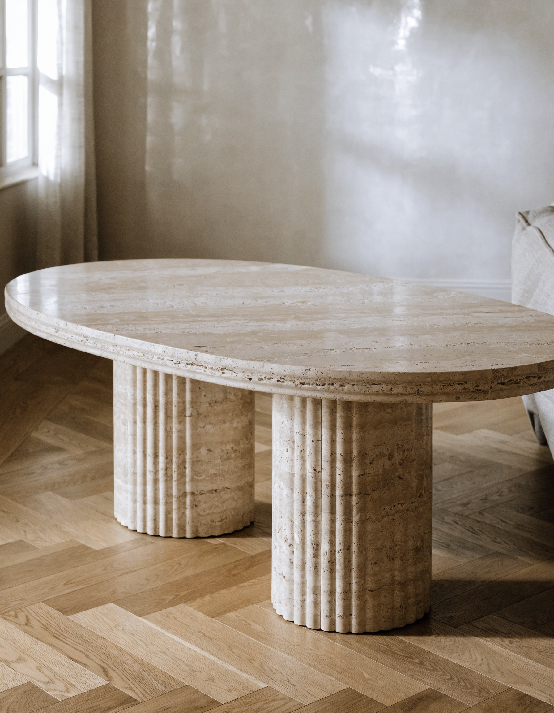 The Fluted Oval Travertine Coffee Table in living room — herringbone oak floor, fluted column detail