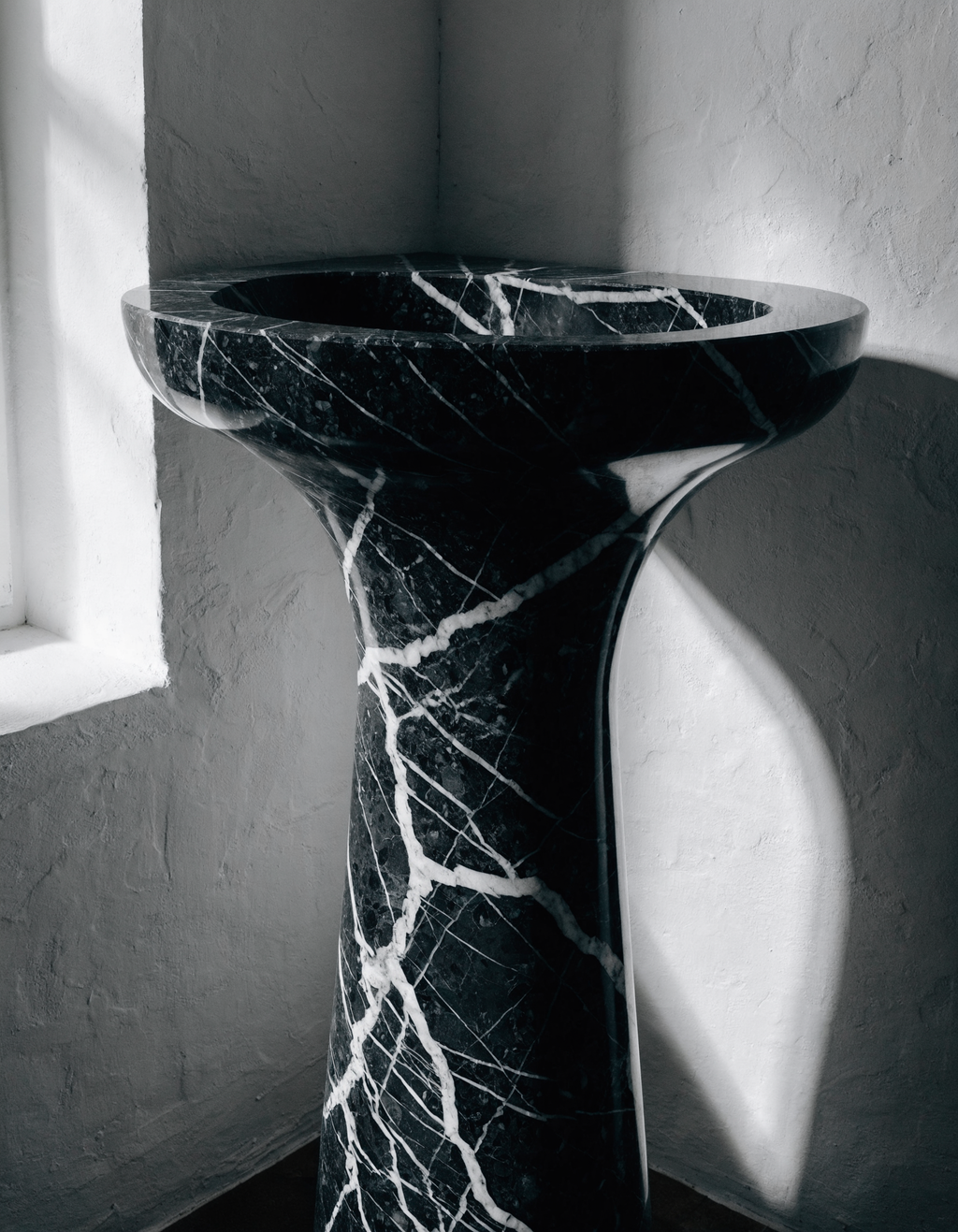 The Monolith Basin in spare dark bathroom — white plaster walls contrast with absolute black marble