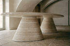 The Oval Travertine Dining Table in dining space — arched plaster ceiling, warm stone floor, Italian editorial